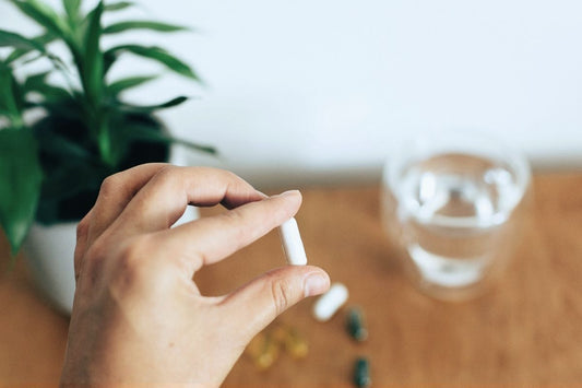 Person holding a white capsule with a glass of water nearby, representing precise daily lithium orotate dosing